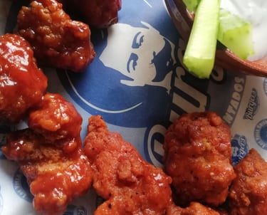 Boneless de pollo bañados en salsa BBQ sobre papel de grado alimenticio, acompañados de aderezo .