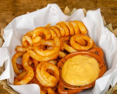 Papas fritas en espiral, crujientes y sazonadas, servidas en una cesta con una salsa cremosa.