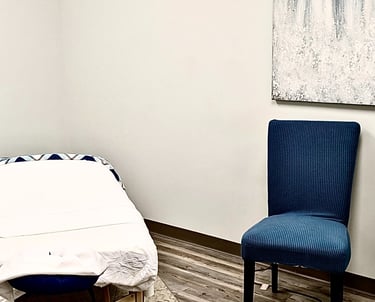 Professional massage therapy room featuring an Earthlite table, a blue chair, and abstract wall art.