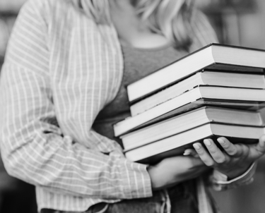 Kobieta w rękach trzyma stos książek.