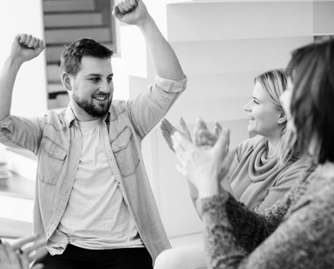 Mężczyzna unosi ręcę w górę, obok dwie kobiety biją brawo.