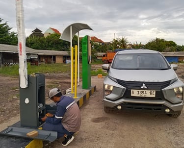 A technician repairs a parking lot boom gate system next to a silver Mitsubishi Xpander car.