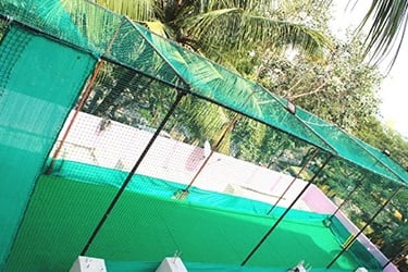 Workers carefully fitting a green safety net around a school rooftop sports area with city buildings