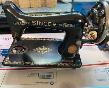 Vintage black Singer sewing machine with gold floral decals resting on a USPS Priority Mail box.
