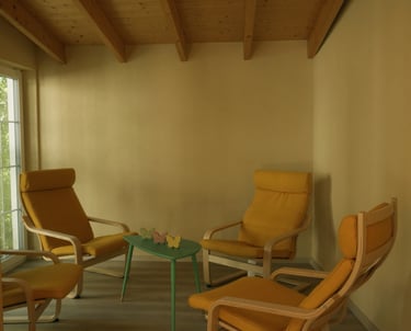 Gemütlicher Innenraum mit vier gelben Sesseln und einem kleinen grünen Tisch unter einer Holzdecke.