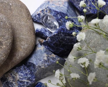 Cristales naturales de sodalita azul y piedras de río pulidas combinadas con flores blancas.