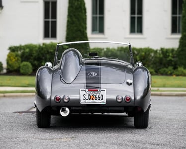 Photograph of a silver and black 1958 MG MGA from the rear in a elegant garden setting