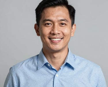 A professional corporate headshot of a friendly Southeast Asian / Indonesian man in his 30s wearing a light blue shirt. He has a warm smile and is positioned against a simple, light gray studio background. The style is modern, sharp, and clean.