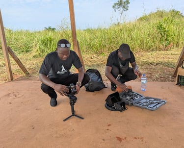Two videographers set up professional camera equipment and a gimbal stabilizer for an outdoor field shoot.