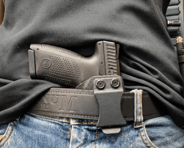 Black handgun in an IWB kydex holster for concealed carry on a leather belt.