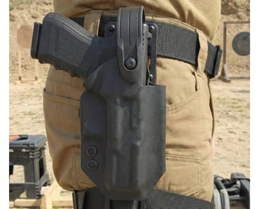 Close-up of a black tactical handgun holster mounted on a duty belt at a firing range.