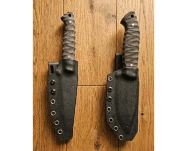 Two custom fixed blade knives with textured G10 handles in black Kydex sheaths on a wooden surface.