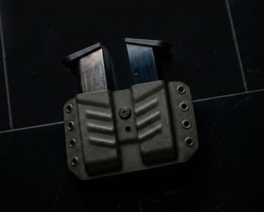 Double magazine pouch in olive drab Kydex holding two handgun mags on a black surface.