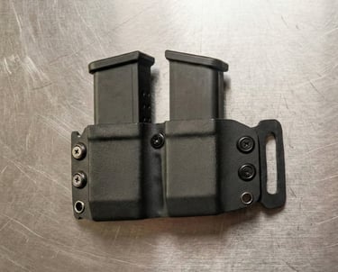 Black dual magazine pouch made of Kydex material holding two handgun magazines on a metal surface.