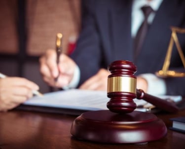 Professional lawyer in a suit signing legal documents next to a wooden judge gavel and scales of justice.