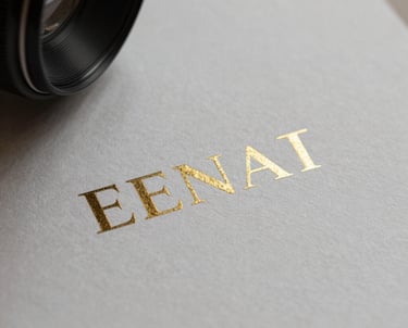 Photography of luxury printed business materials with a sharp focus on metallic foil logos and textured paper.