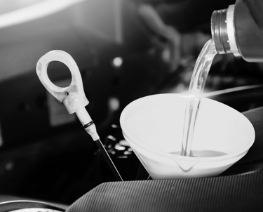 Pouring fresh synthetic motor oil through a funnel into a car engine during a routine oil change.