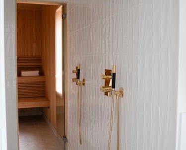 Modern luxury walk-in shower with gold fixtures and white subway tile next to a wood-paneled home sauna.