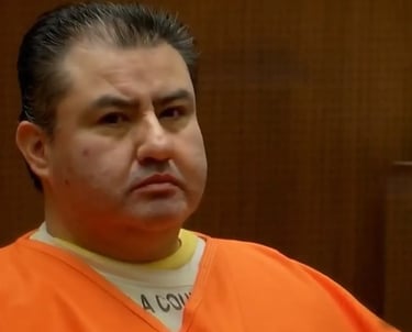 A man in an orange prison jumpsuit sits in a courtroom during a legal hearing.