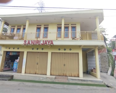 Saniri Jaya storefront in Indonesia with yellow two-story building and metal rolling doors.