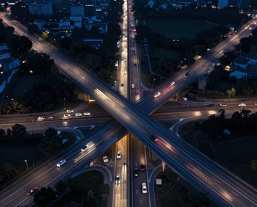 Symmetrical drone shot of a modern French highway intersection at night, showing streaks of light from cars. Deep steel blue and dark blue palette.