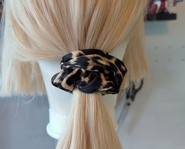 Blonde hair tied in a low ponytail using a trendy leopard print fabric scrunchie on a mannequin head.