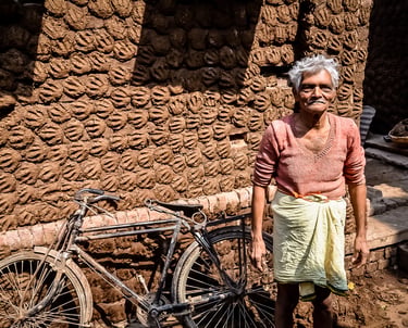 Showing his work of cow dung paddies for fuel drying in the sun against a wall in Varanasi, India.