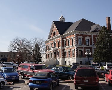 Historic brick courthouse with a white clock tower and parking lot full of cars Macomb IL