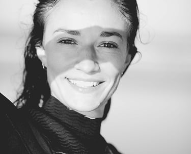 a woman in a wetsuit smiling and holding a surfboard