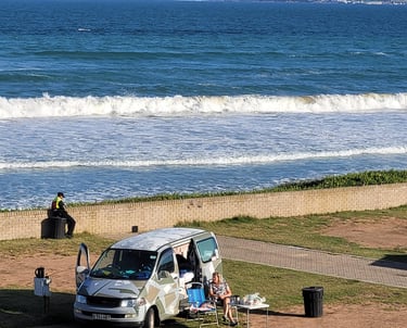 a van parked on the beach with people sitting in chairs