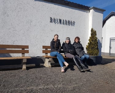 Three women sitting on a bench outside the Rosmarhof equestrian facility on a sunny day.