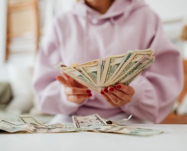 A woman in a pink hoodie, sitting at a tble and counting money.
