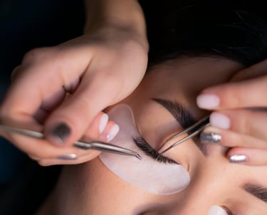 Lashista aplicando extensiones de pestañas a una modelo con parche en cara