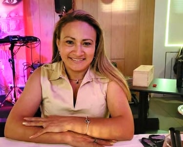 Smiling woman with blonde hair sitting at a dinner table in a restaurant with warm lighting.