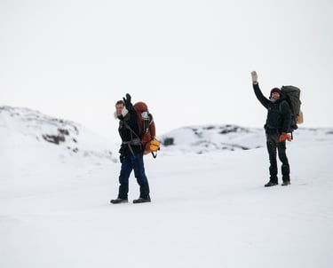 Deux randonneurs avec des sacs à dos font signe de la main en traversant un paysage hivernal enneigé