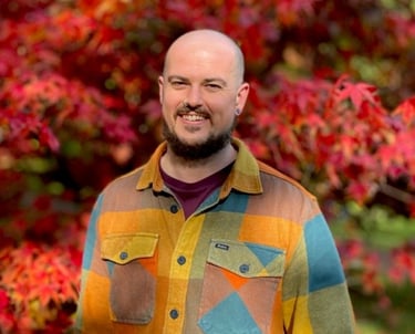 Sam rayes creative bio pic smiling with autumnal trees as a background