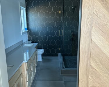 Modern bathroom featuring black hexagon wall tiles, a glass walk-in shower, and a light wood vanity.