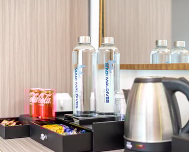 Madi Maldives hotel room amenities with bottled water, electric kettle, and snack tray.