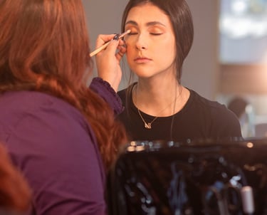 Maquilladora profesional que aplica sombra de ojos dorada a una modelo usando un pincel difuminador.