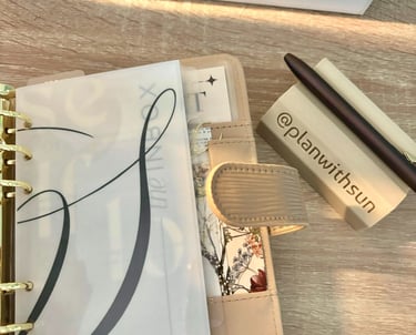 Aesthetic beige ring planner with vellum dividers and a pen rest on a wooden desk.