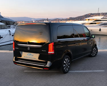 Black Mercedes V-Class luxury van parked at a harbor with yachts during sunset.