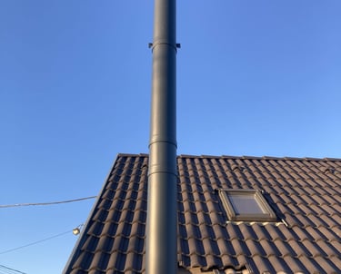 Családi ház barna cseréppel fedett tetején antracit színű, korrózióálló acélból készült kémény.