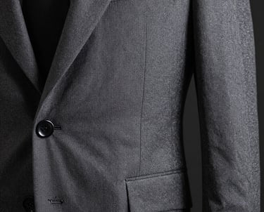 Detail of a tailored grey suit fabric against a dark background. High resolution texture, professional and premium feel. Desaturated tones.