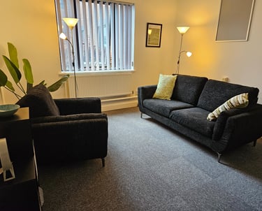 Modern therapy room with a dark grey sofa and armchair on grey carpet floor.