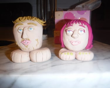 Handmade clay figurines of a man and woman with large feet sitting on a marble counter.