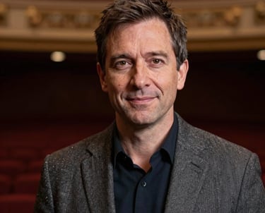 A professional headshot of a creative director in a sophisticated theater environment. The lighting is soft and flattering, emphasizing a mood of professional integrity and artistic passion. North American / Pacific Northwest US style attire.