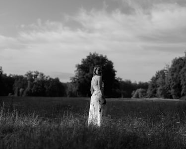 Black and white outdoor portrait of a woman in a floral maxi dress standing in a grassy field.