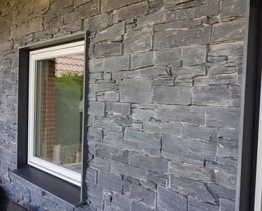 Moderne ydervæg på hus med grå stablet stenbeklædning og hvidindrammede vinduer.