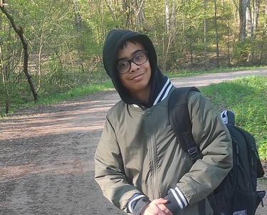 a man in a jacket and glasses standing on a dirt road