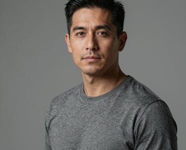 Professional portrait of a man with a confident, calm expression in a minimalist studio. Muted gray attire, soft lighting. Hispanic / Japanese-inspired aesthetic.